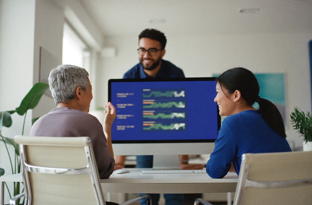 An agency team gathers around a monitor showing campaign charts.